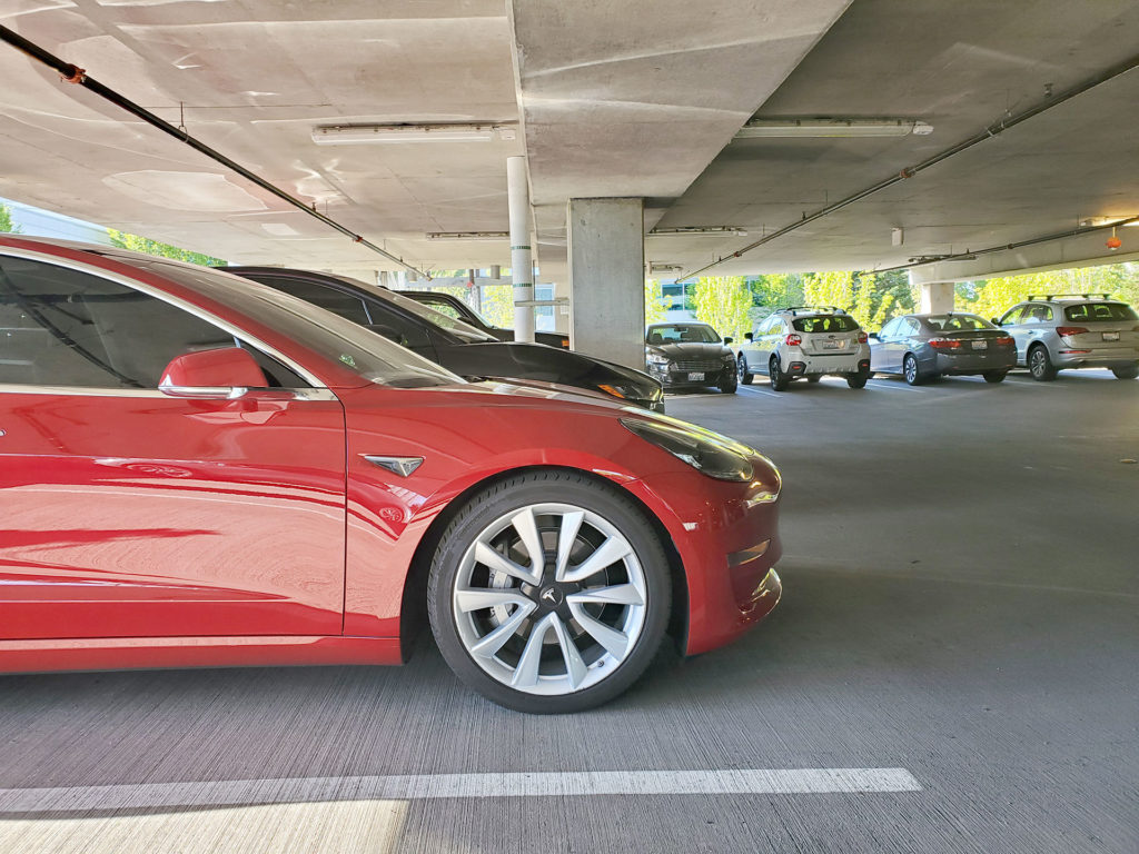 Tesla Model 3 and Jaguar I-Pace standing side-by-side in a parking lot - front side angle from the Model 3 comparing length.