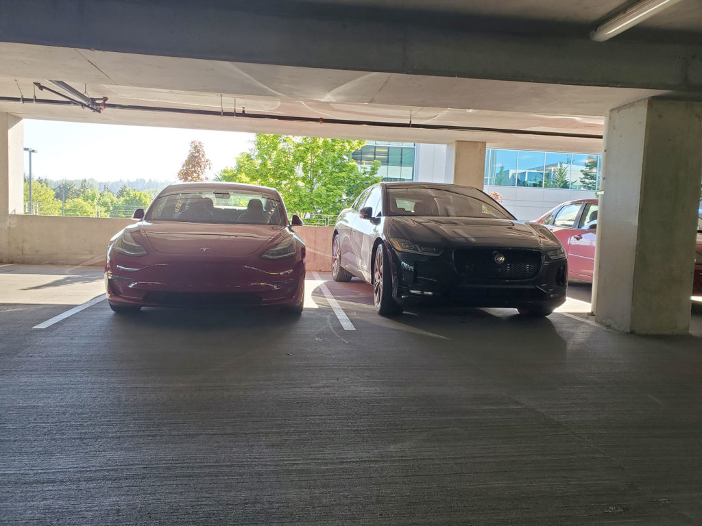 Tesla Model 3 and Jaguar I-Pace standing side-by-side in a parking lot - front angle.