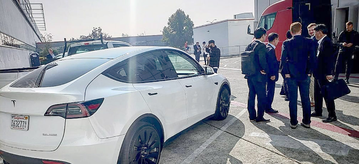 Tesla Model Y Performance with black wind turbine wheels spotted at the Tesla Fremont car factory, red Tesla Semi in the background.