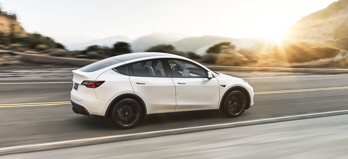 White Tesla Model Y cruising on highway at sunset. Production started in Jan 2020, deliveries expected Mar 2020 as per Q4' 2019 Earnings Call.