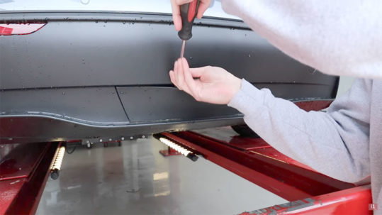 Finding the Tesla Model Y tow hitch under the rear diffuser panel.